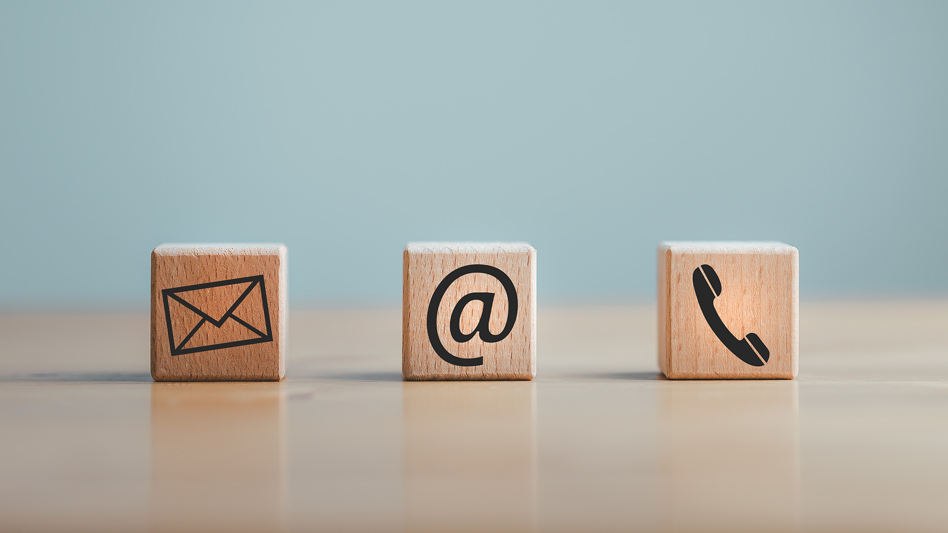 The image shows four wooden blocks each with an icon representing a different mode of communication  email, phone, chat, and mail.