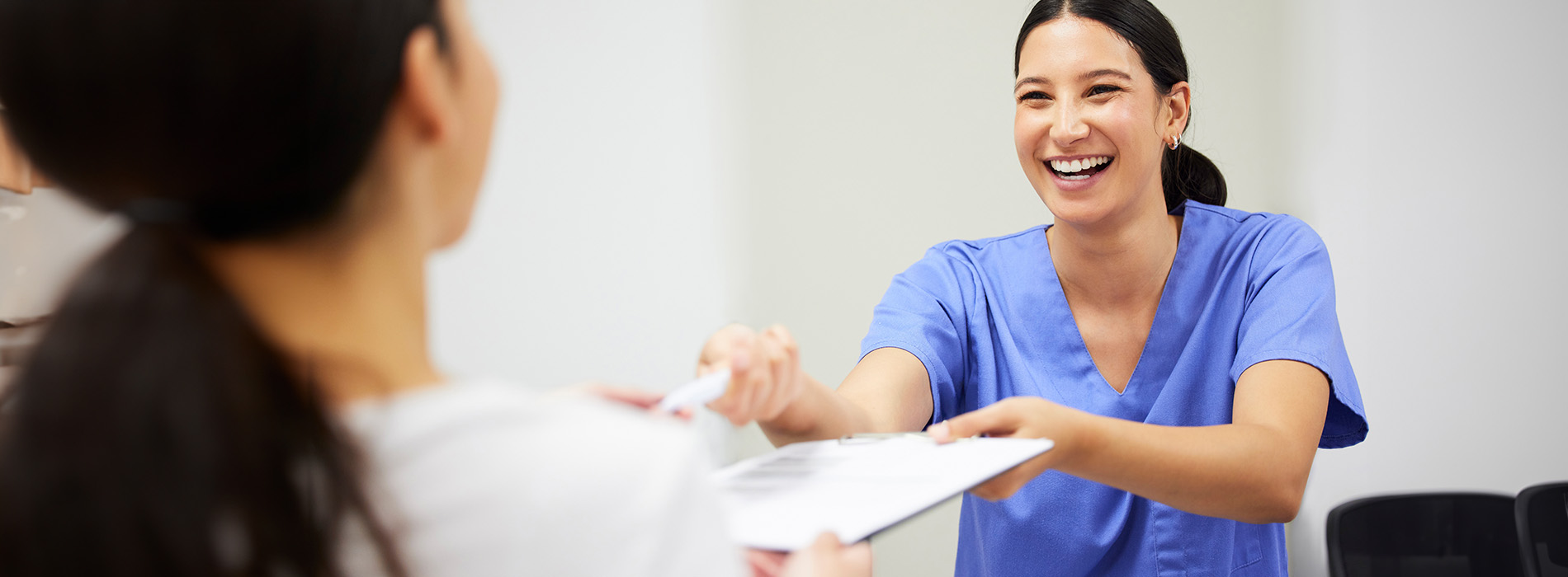 In the image, there is a smiling woman in scrubs handing over a card to another person who appears to be receiving it with anticipation.