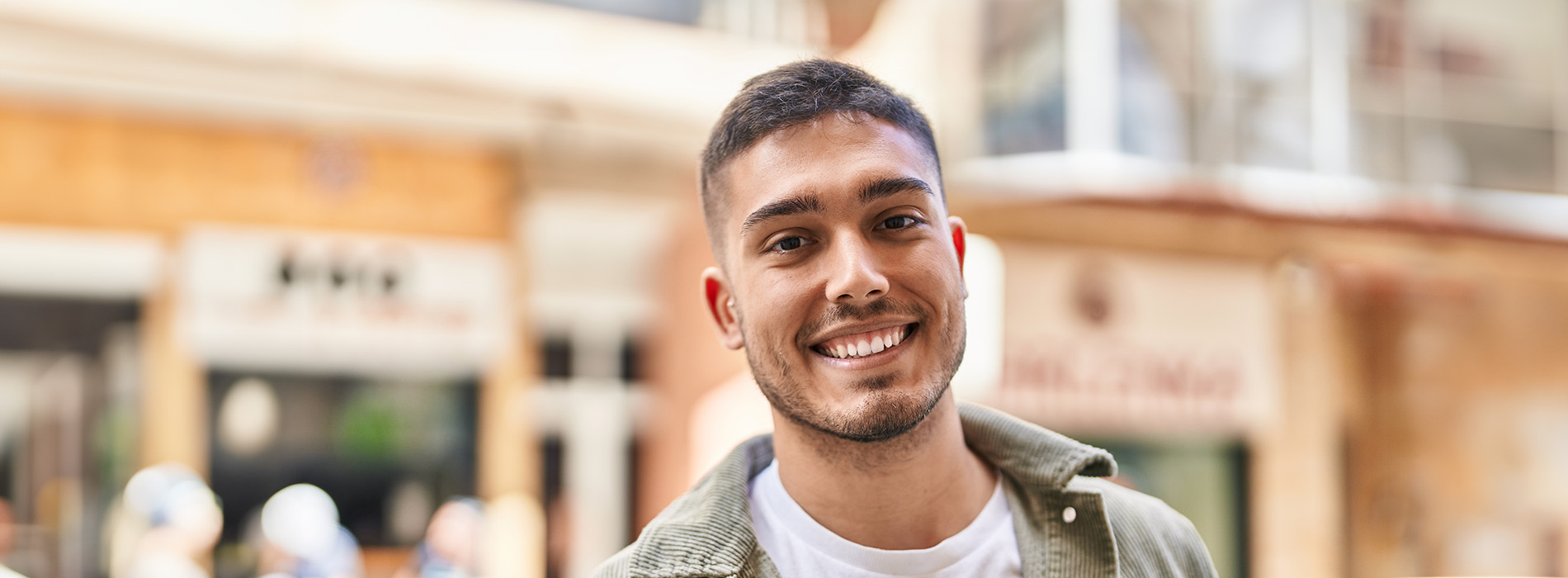 A young man with a beard stands confidently in front of a city street backdrop.