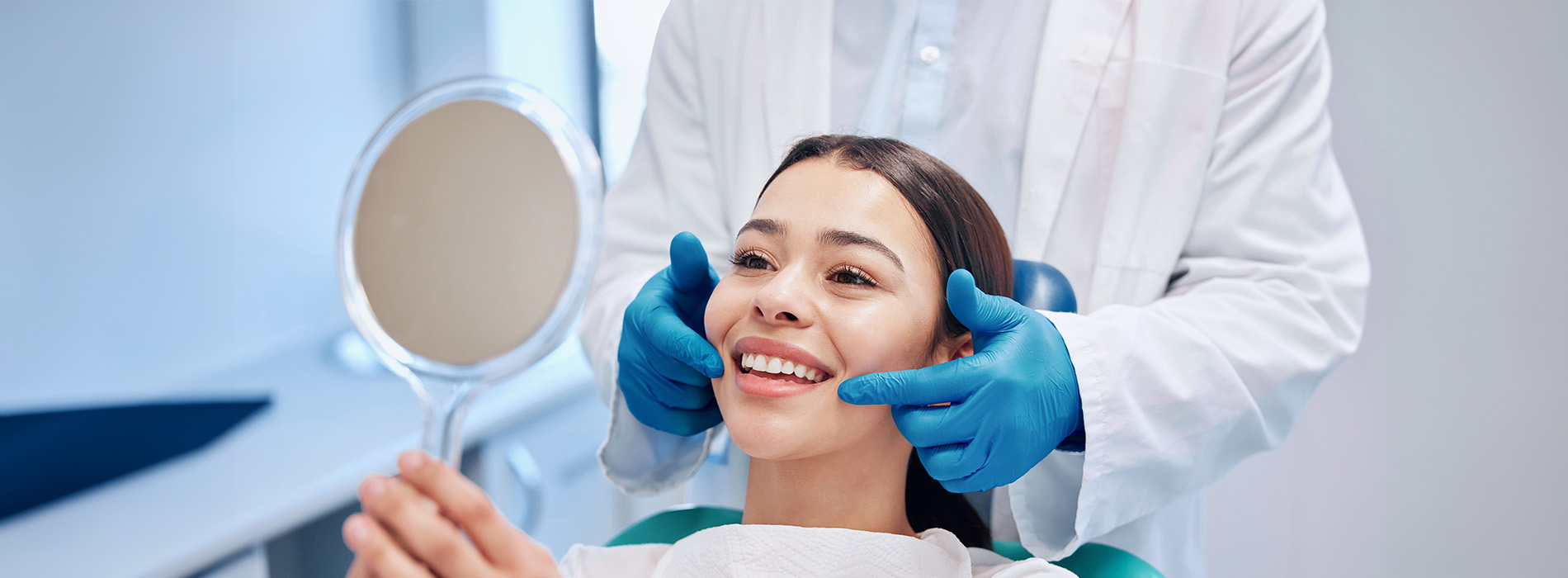 A person sitting in a dental chair with a dentist performing an examination, both wearing blue gloves and medical masks.