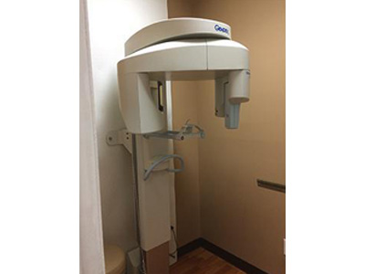 The image depicts a dental X-ray machine situated within an indoor setting, possibly a dental office or clinic.