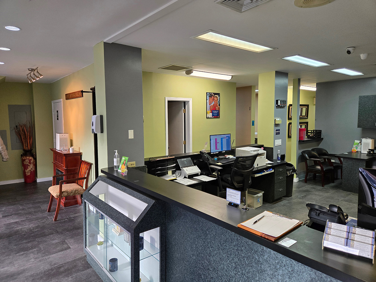 The image shows an interior view of a well-lit office space with a reception desk, chairs, and a countertop displaying various items.