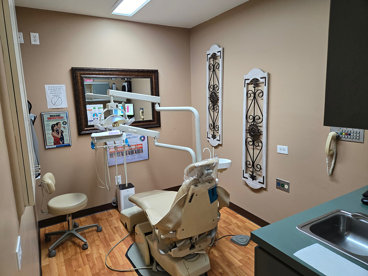 The image shows a dental office interior with a dental chair, a dental mirror, a dental light, and various other dental equipment.
