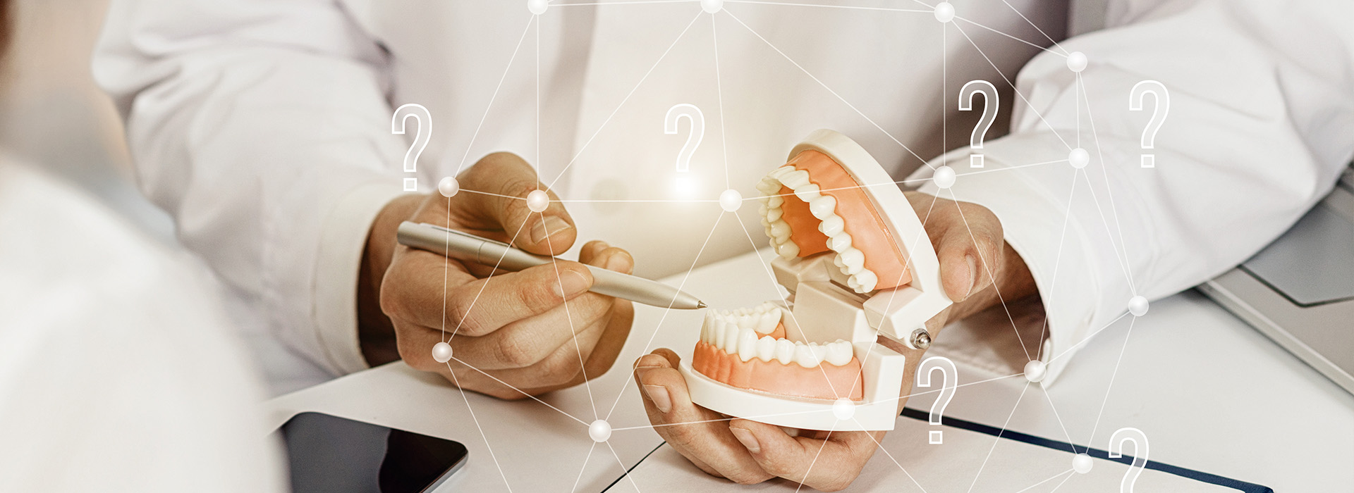 A person s hand holding a smartphone with a dental model displayed on its screen, set against a blurred background featuring a medical professional and digital information.