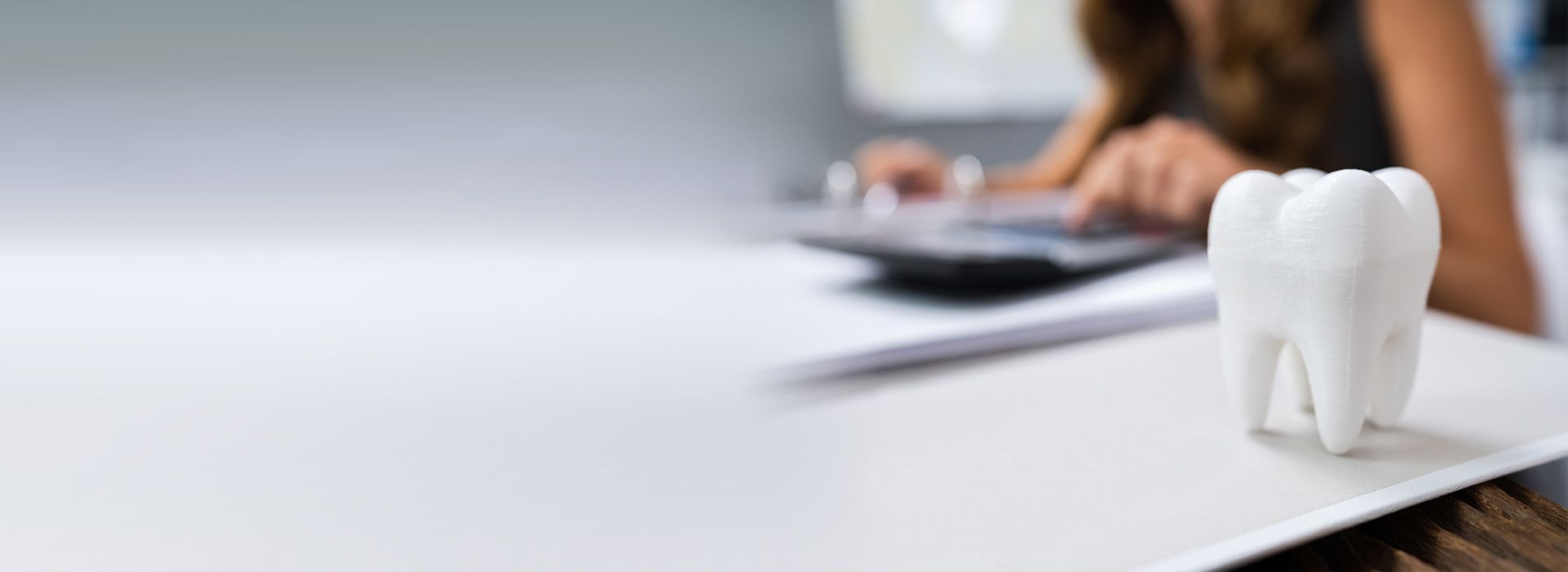 A person working at a desk with a computer monitor, keyboard, and mouse, set against a blurred background featuring an office environment.