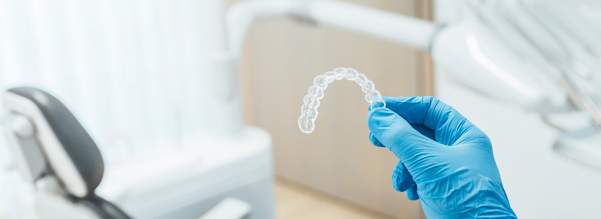 A medical professional wearing gloves holds up a transparent dental implant model.