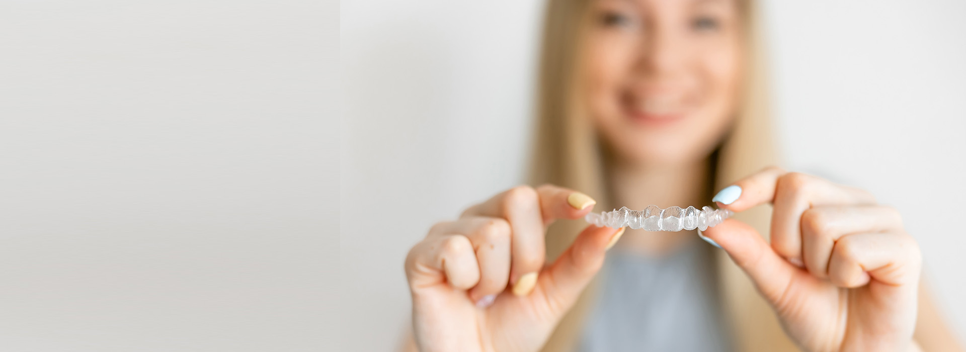 A smiling woman holding up a ring with her left hand against a blurred background.