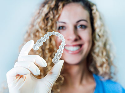 Woman holding up a clear plastic mouthguard with a smile on her face.