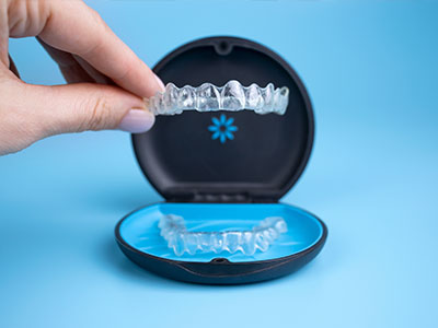 The image shows a person s hand holding an open box containing a set of clear aligners, which are dental braces used for orthodontic treatment.