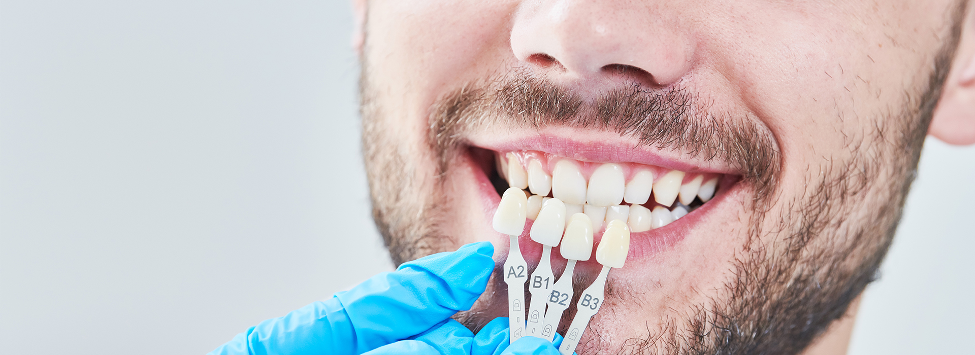 A man with a toothpick in his mouth smiling at the camera while holding dental tools.