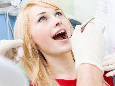 A woman receiving dental care from a dentist, with her mouth open and a dental tool in use.