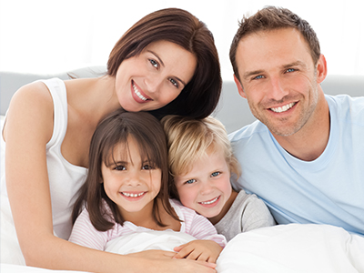 A family of four adults and two children posing together on a bed.