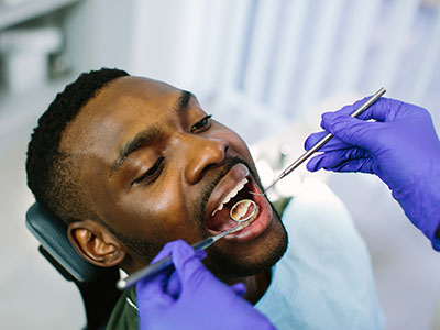 A person undergoing dental treatment with a dentist using tools, wearing protective gloves and a face mask.