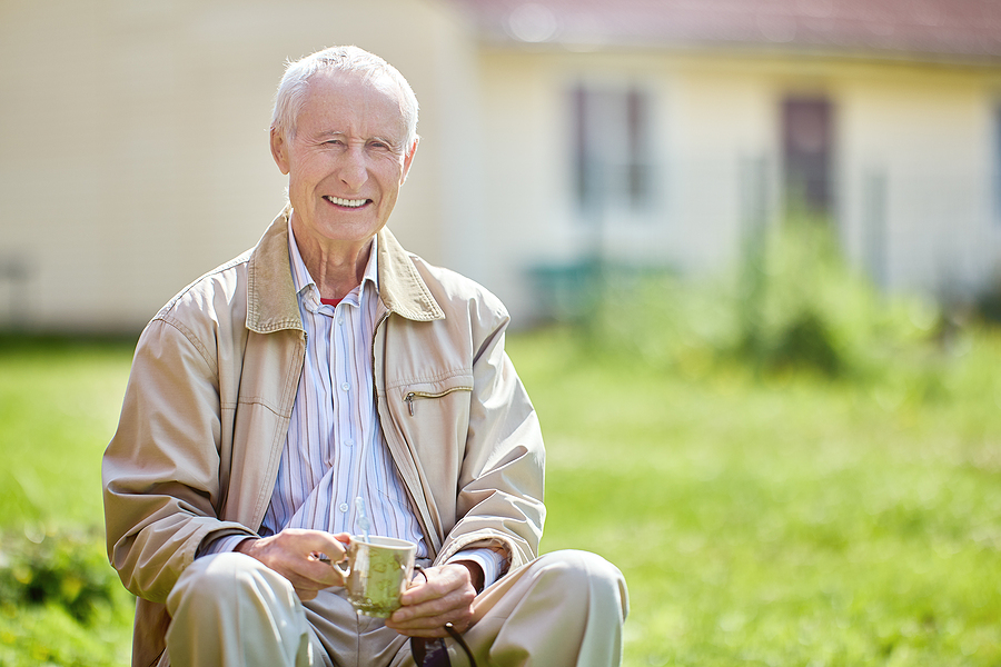 Smiling senior man with straight, white teeth sitting outside and drinking tea. Senior oral care concept