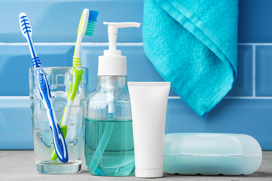 Toothbrushes in a glass on a bathroom countertop next to hand soap and a tube of toothpaste - dental hygiene routine concept