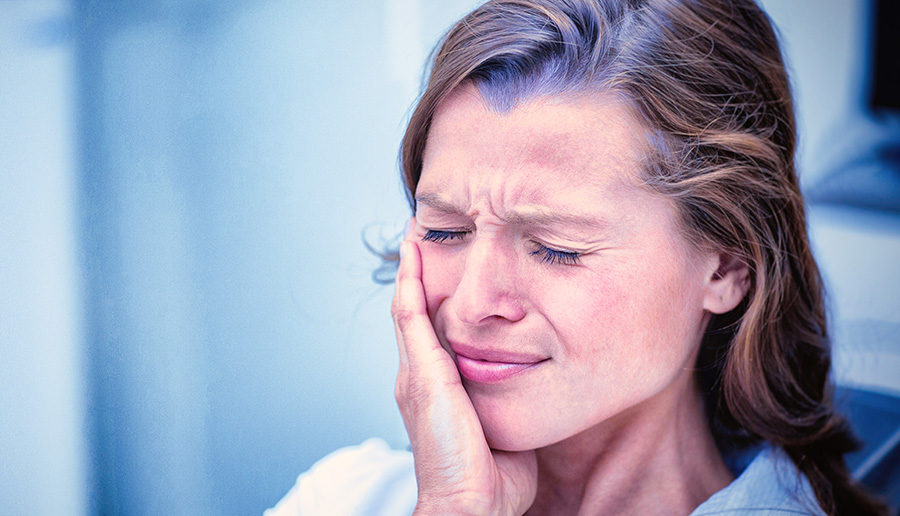 woman in pain from a toothache clutching face and wincing